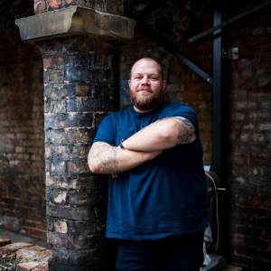 Billy Darroch is a Director at Kan Do Ventures and specialises in supporting msall businesses. Billy is leaning against a brick column and is wearing a navy polo shirt. His arms are crossed and he is smiling.
